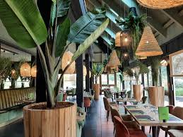 Installez-vous dans notre grande salle à la décoration noire et verte, ornée de palmiers et baignée de lumière naturelle avec à sa mezzanine. Profitez également de notre terrasse extérieure pour vos repas en été et de notre patio.